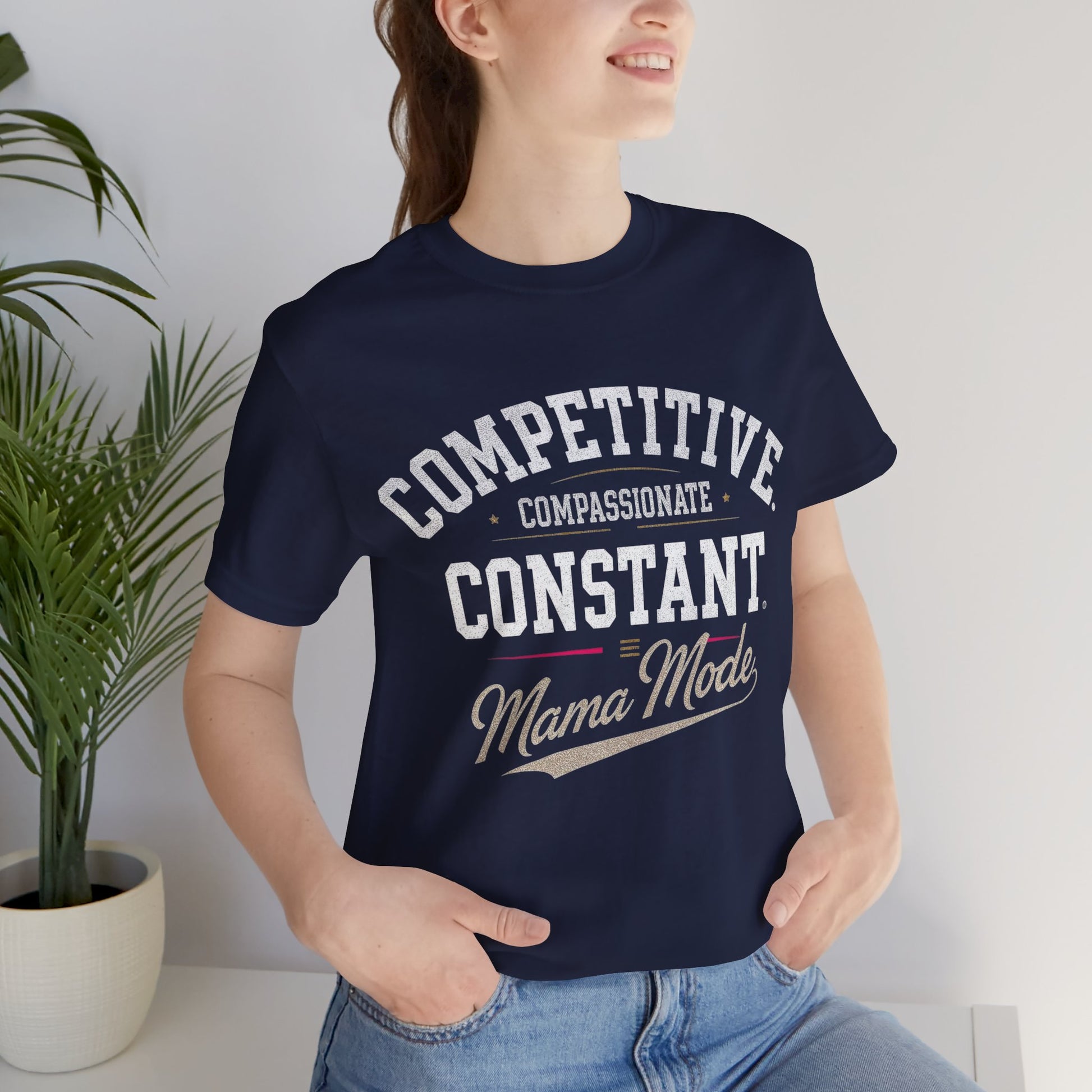 Person wearing a navy blue t-shirt with text, COMPETITIVE, COMPASSIONATE, CONSTANT = MAMA MODE.