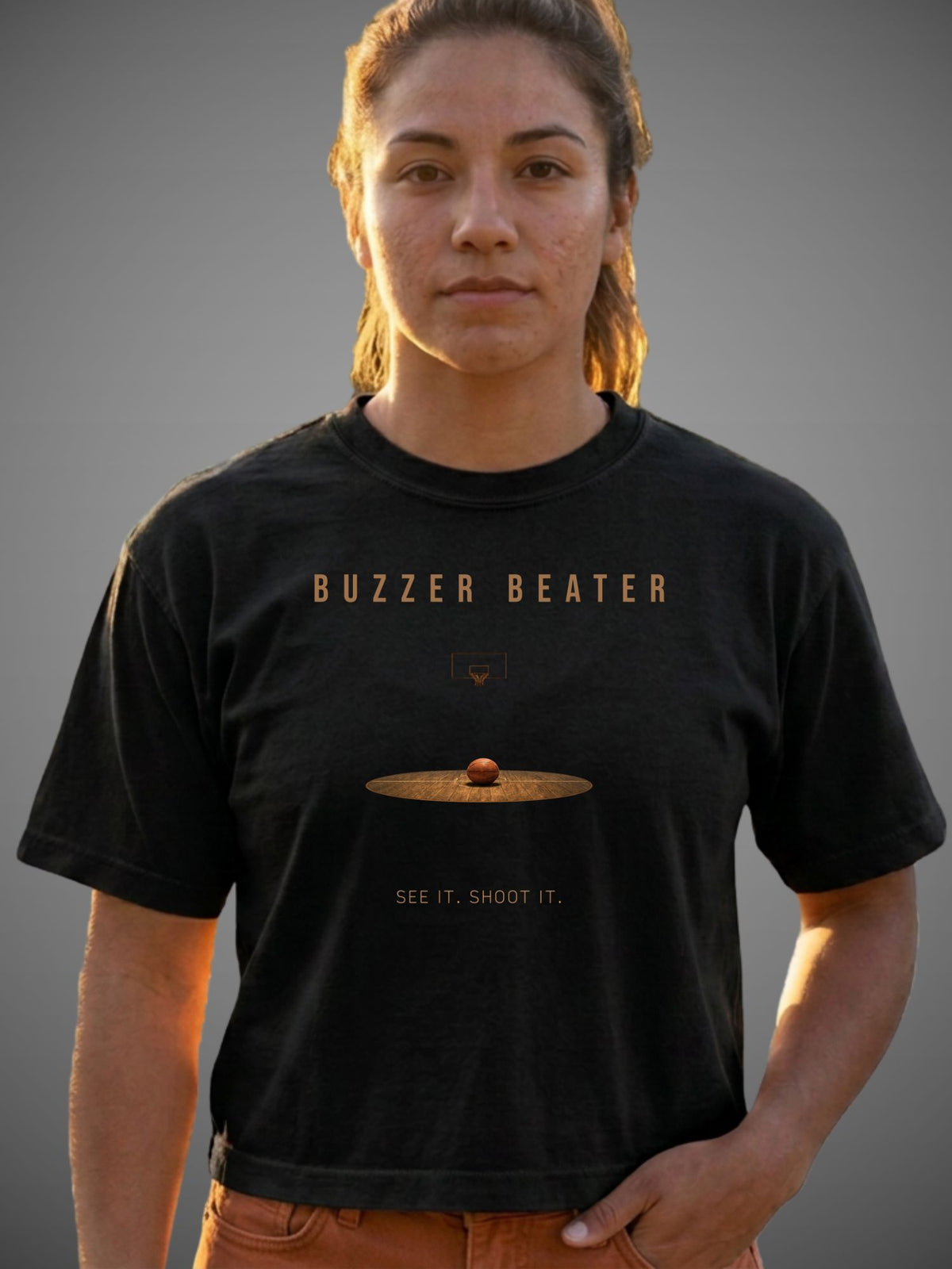 A woman wearing a black graphic t-shirt with the text 'BUZZER BEATER' and 'SEE IT. SHOOT IT.