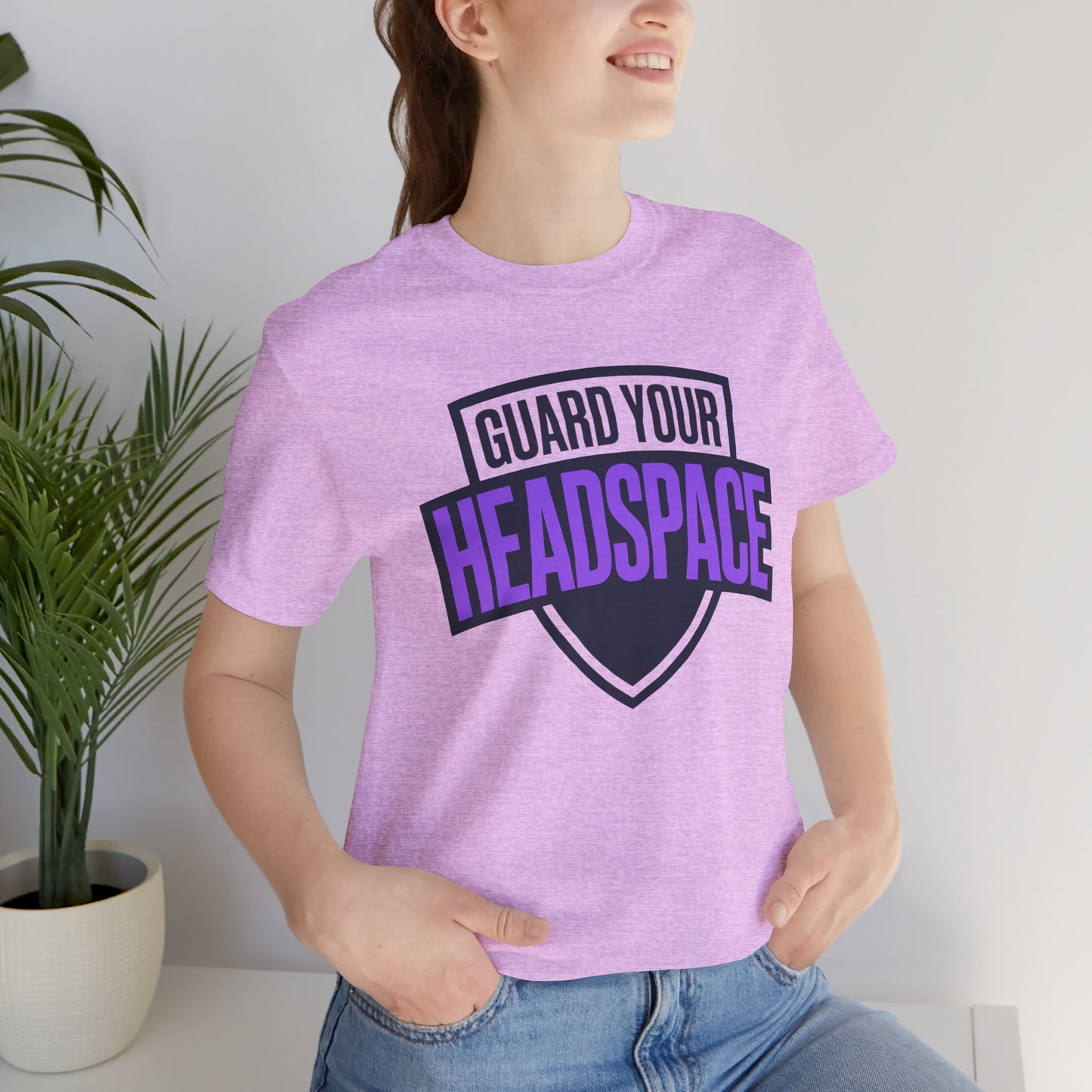 Person wearing a purple t-shirt with 'Guard Your Headspace' text, standing indoors next to a plant.