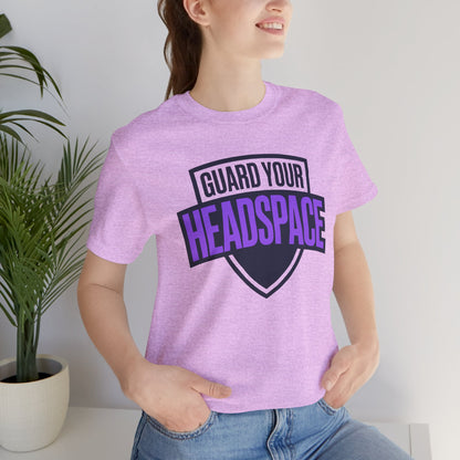 Person wearing a purple t-shirt with 'Guard Your Headspace' text, standing indoors next to a plant.