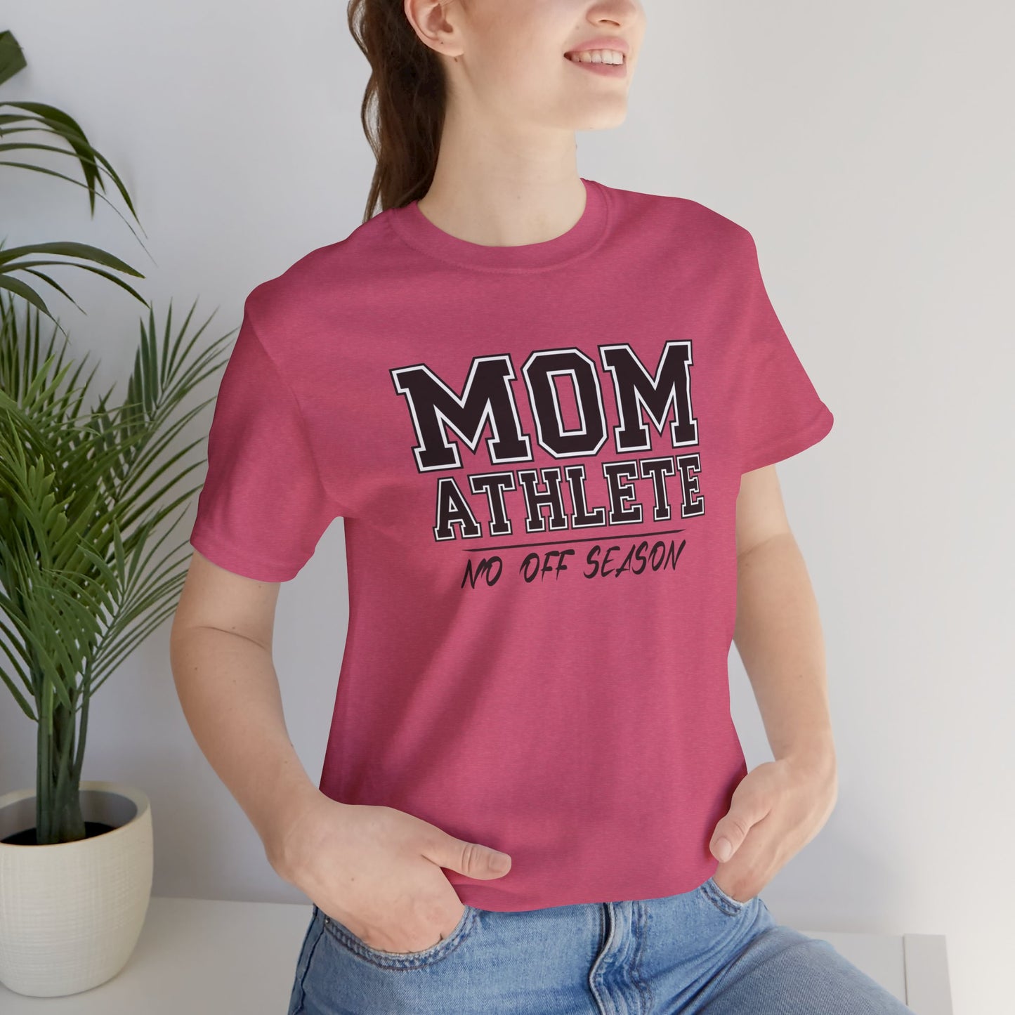 Person wearing a pink t-shirt with 'Mom Athlete No Off Season' text, standing indoors.