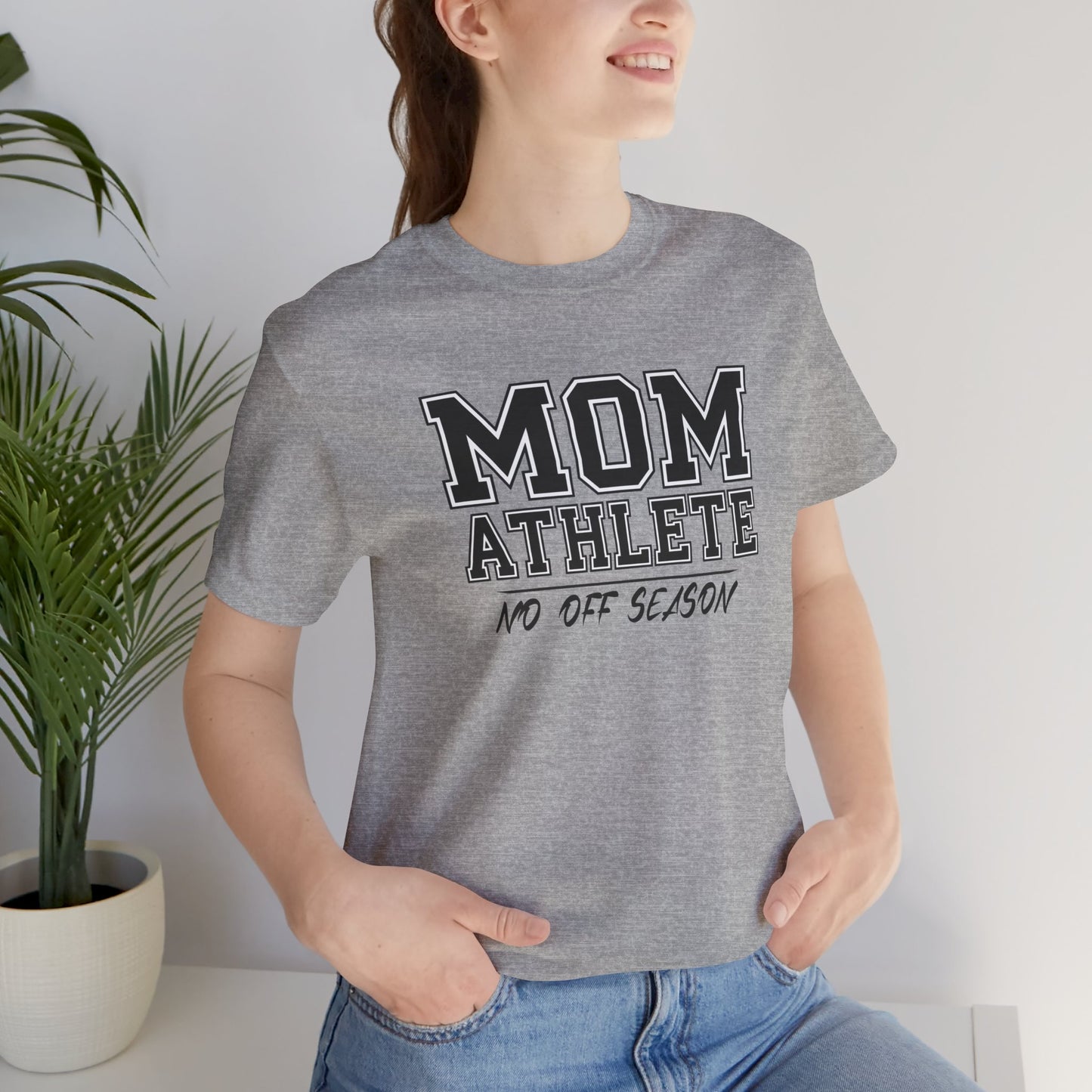 Person wearing a gray t-shirt with 'Mom Athlete No Off Season' text, standing indoors with a plant in the background.
