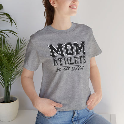 Person wearing a gray t-shirt with 'Mom Athlete No Off Season' text, standing indoors with a plant in the background.